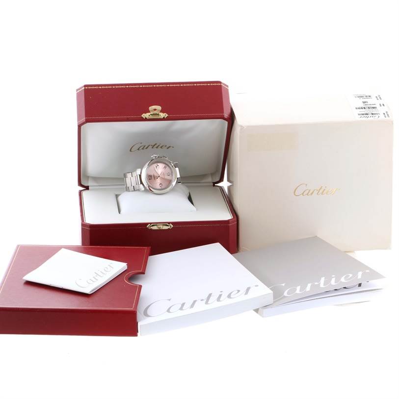 The image shows a Cartier Pasha W31075M7 Women
s Stainless Steel Pink Dial W31075M7 Women
s Stainless Steel Pink Dial watch in its open case, along with a white outer box and accompanying booklets.