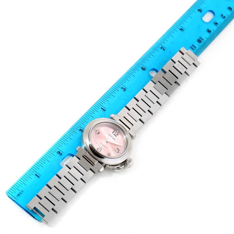 The image shows a Cartier Pasha W31075M7 Women
s Stainless Steel Pink Dial W31075M7 Women
s Stainless Steel Pink Dial watch with a pink dial, silver bracelet, and placed next to a blue ruler for scale.