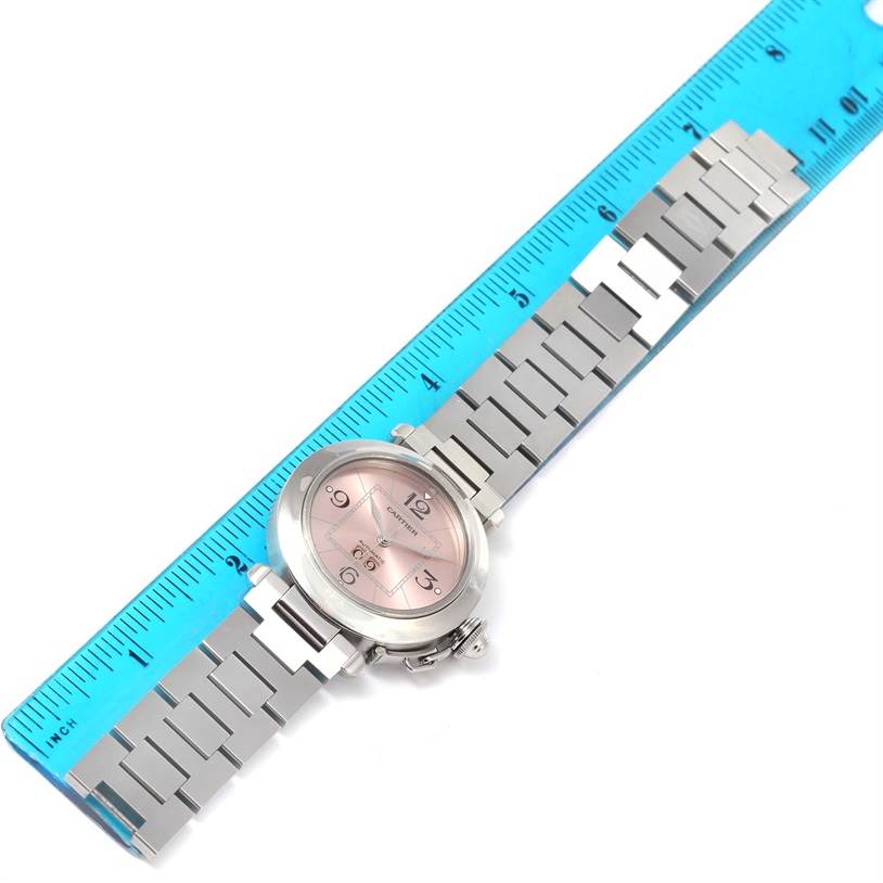 The image shows the top view of a Cartier Pasha W31058M7 Women's Stainless Steel Pink Dial W31058M7 Women's Stainless Steel Pink Dial watch along a ruler, highlighting the watch face and metal bracelet.