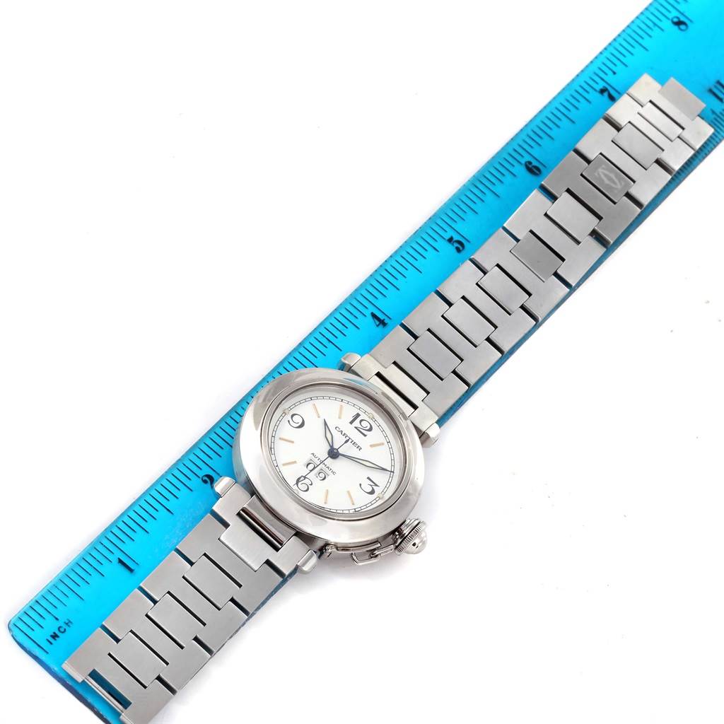 The Cartier Pasha W31044M7 Men's Stainless Steel White Dial W31044M7 Men's Stainless Steel White Dial watch is shown from a top-down angle, displaying the full face and metal bracelet with a blue ruler beside it for scale.
