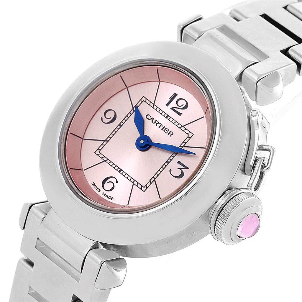 The image shows a close-up view of the Cartier Pasha W3140008 Women's Stainless Steel Pink Dial W3140008 Women's Stainless Steel Pink Dial watch, highlighting its pink dial, blue hands, and crown set with a pink stone, partially on its metal bracelet.