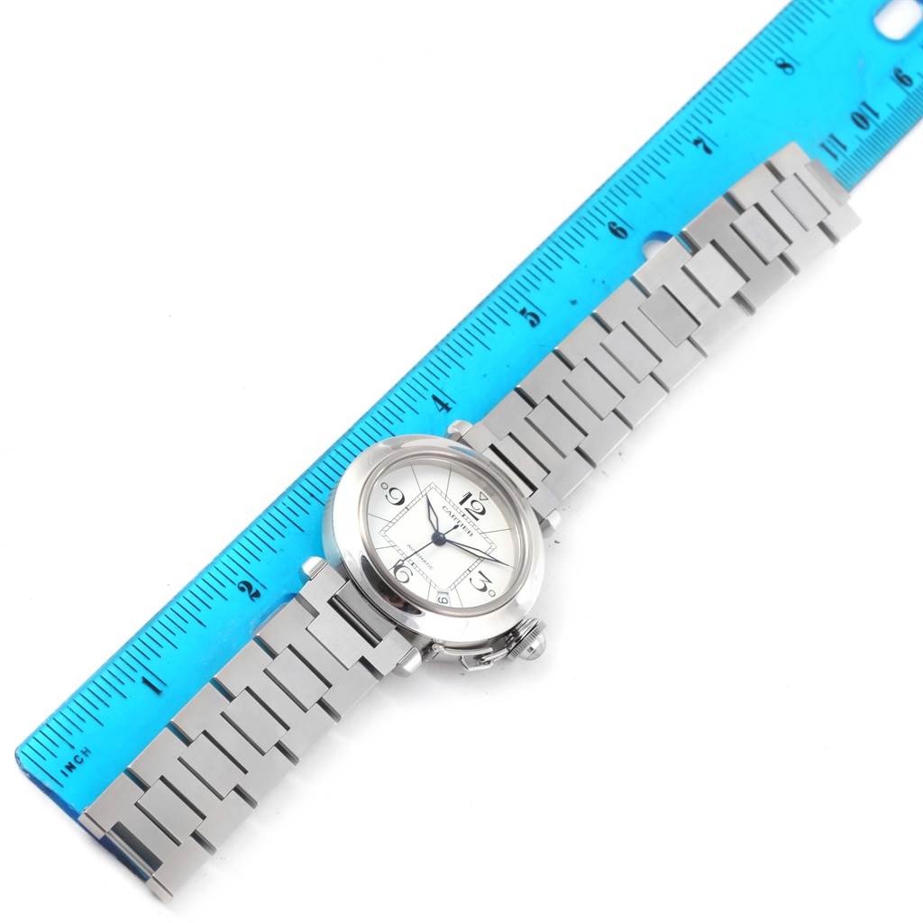 The Cartier Pasha W31074M7 Women's Stainless Steel White Dial W31074M7 Women's Stainless Steel White Dial watch is shown flat with its silver bracelet, dial, and crown, alongside a blue ruler for scale.