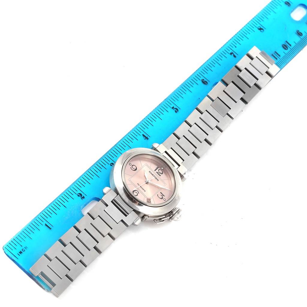 The Cartier Pasha W31075M7 Women
s Stainless Steel Pink Dial W31075M7 Women
s Stainless Steel Pink Dial watch is shown lying flat with its stainless steel bracelet extended alongside a blue ruler.