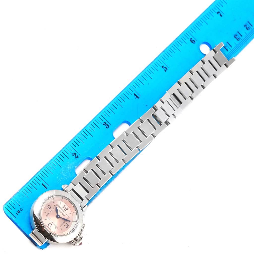 The image shows a Cartier Pasha W3140008 Women's Stainless Steel Pink Dial W3140008 Women's Stainless Steel Pink Dial watch from a top-down angle, featuring its face and metal bracelet next to a blue ruler.