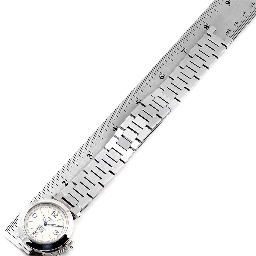 The Cartier Pasha W31044M7 Men's Stainless Steel White Dial W31044M7 Men's Stainless Steel White Dial watch is shown angled diagonally, featuring its face and entire metal wristband placed alongside a ruler.