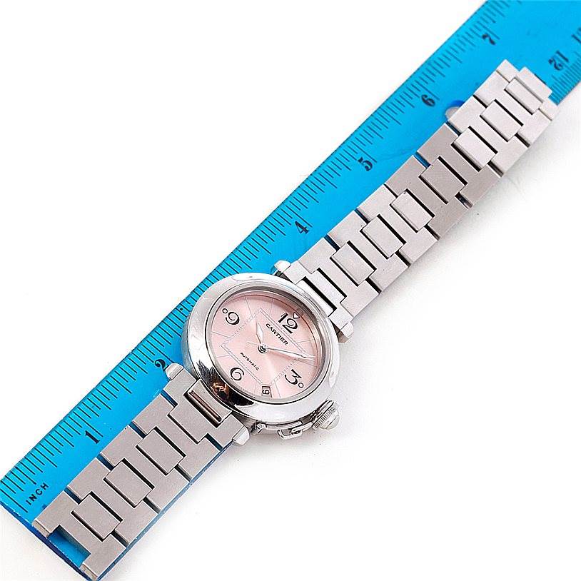 The Cartier Pasha W31075M7 Women
s Stainless Steel Pink Dial W31075M7 Women
s Stainless Steel Pink Dial watch is shown flat from above, next to a blue ruler, displaying the watch face and metal bracelet.
