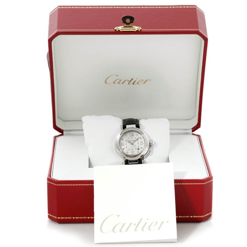 The Cartier Pasha WJ11902G Women's White Gold Silver Dial WJ11902G Women's White Gold Silver Dial watch is displayed in a red Cartier box, with its face, black strap, and a Cartier card visible.