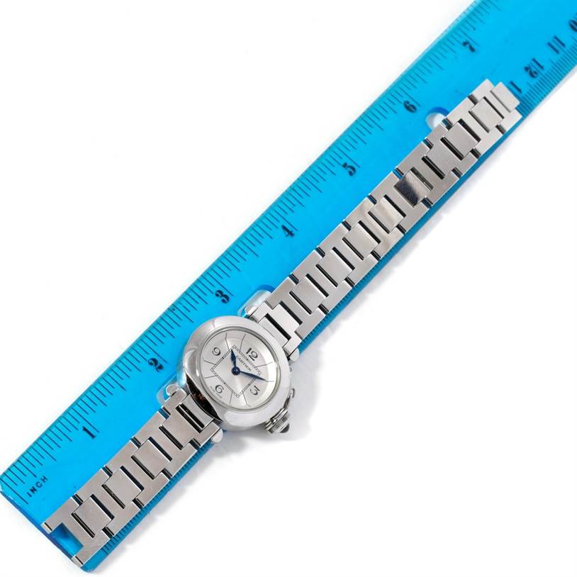 The image shows a Cartier Pasha W31043M7 Women
s Stainless Steel Silver Dial W31043M7 Women
s Stainless Steel Silver Dial watch laid flat alongside a blue ruler, highlighting its face and metal bracelet.