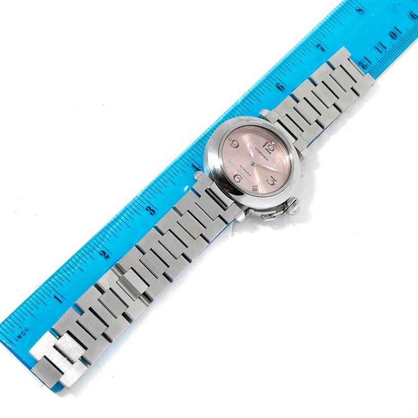 The Cartier Pasha W31075M7 Women
s Stainless Steel Pink Dial W31075M7 Women
s Stainless Steel Pink Dial watch is shown from a top-down angle with its metal strap and face visible, alongside a blue ruler for scale.