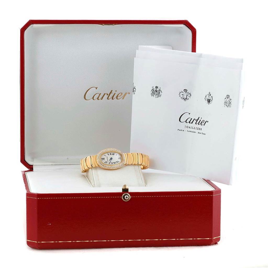 The Cartier Baignoire WB5094D8 Women's Yellow Gold Silver Dial WB5094D8 Women's Yellow Gold Silver Dial watch is displayed at a front angle, placed in its box with accompanying literature in the background.