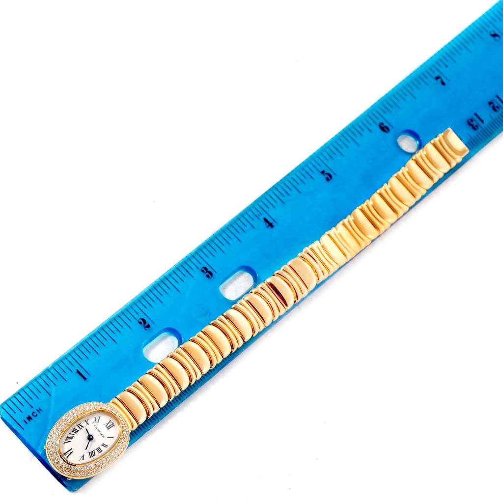 This image shows a Cartier Baignoire WB5094D8 Women's Yellow Gold Silver Dial WB5094D8 Women's Yellow Gold Silver Dial watch with its face and bracelet aligned next to a blue ruler for scale.