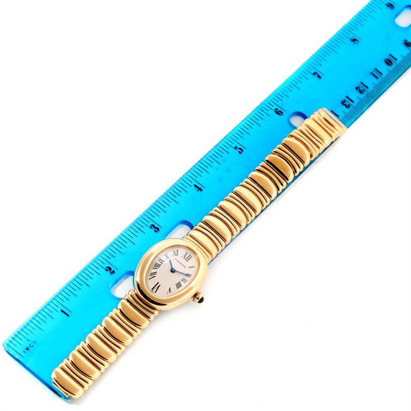 The image shows an overhead view of the Cartier Baignoire Women's Yellow Gold Silver Dial Women's Yellow Gold Silver Dial watch with a gold bracelet placed beside a blue ruler for scale.