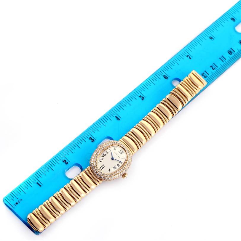 The Cartier Baignoire 1950 Women
s Yellow Gold Silver Dial 1950 Women
s Yellow Gold Silver Dial watch is shown from a top-down angle with a blue ruler measuring its gold bracelet and case.