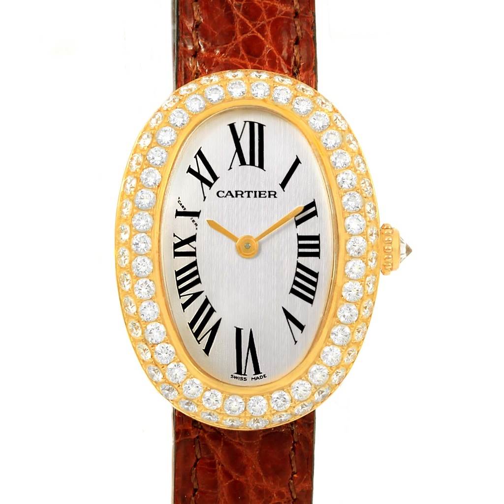 The image shows a Cartier Baignoire 1954 Women
s Yellow Gold Silver Dial 1954 Women
s Yellow Gold Silver Dial watch from a front angle, highlighting its oval face, diamond bezel, and brown leather strap.