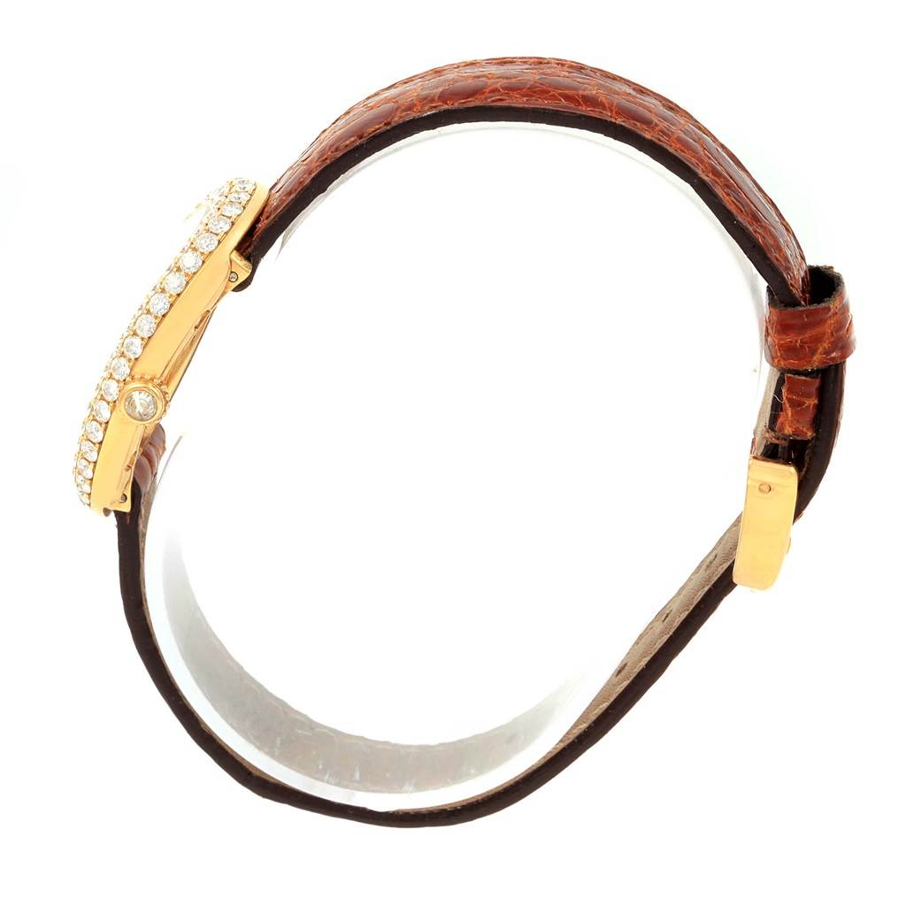 The image shows a Cartier Baignoire 1954 Women
s Yellow Gold Silver Dial 1954 Women
s Yellow Gold Silver Dial watch viewed from the side, highlighting its diamond-encrusted bezel and brown leather strap.