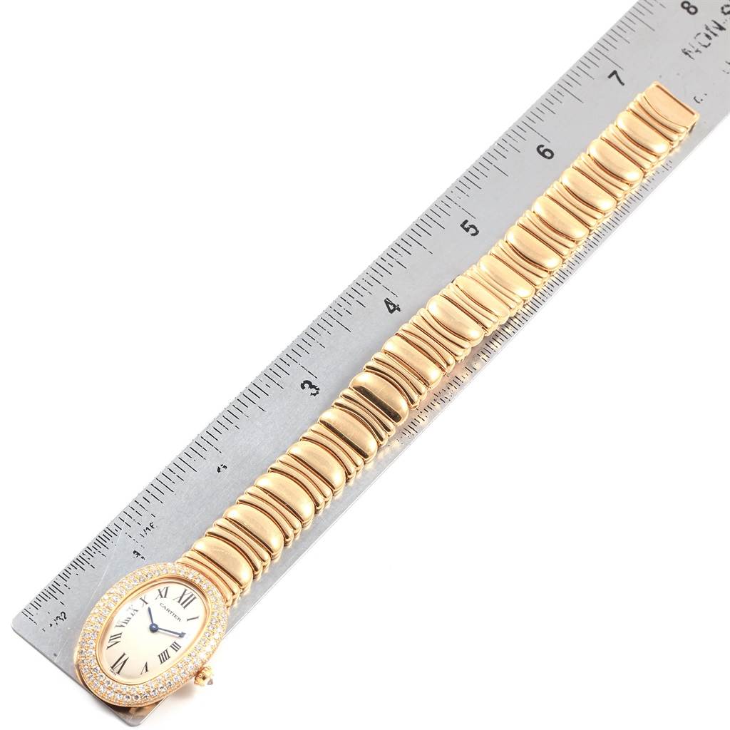 This image shows the Cartier Baignoire 1950 Women's Yellow Gold Silver Dial 1950 Women's Yellow Gold Silver Dial watch laid flat alongside a ruler, displaying the full watch band and the oval-shaped face.