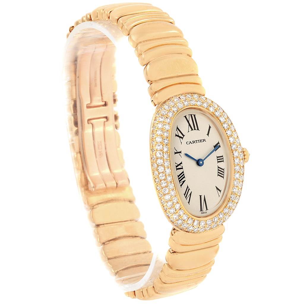 The image shows a Cartier Baignoire 1950 Women's Yellow Gold Silver Dial 1950 Women's Yellow Gold Silver Dial watch at an angle displaying its oval face, diamond bezel, and gold band.