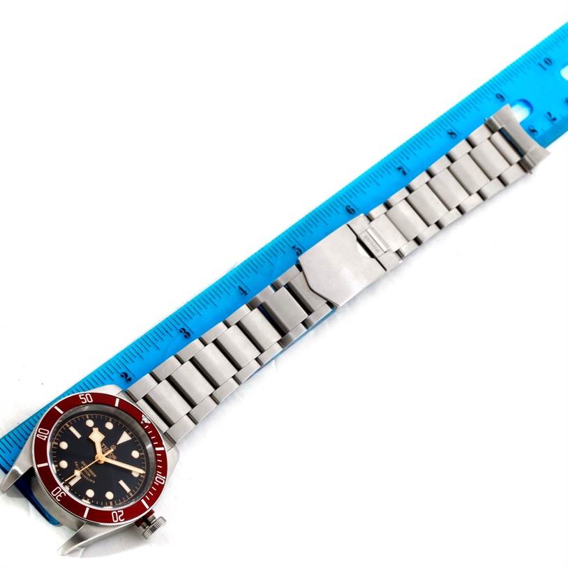 The image shows a Tudor Heritage Black Bay 79220R Men's Stainless Steel Black Dial 79220R Men's Stainless Steel Black Dial watch laid flat, with a blue ruler alongside, displaying the face and metal bracelet.