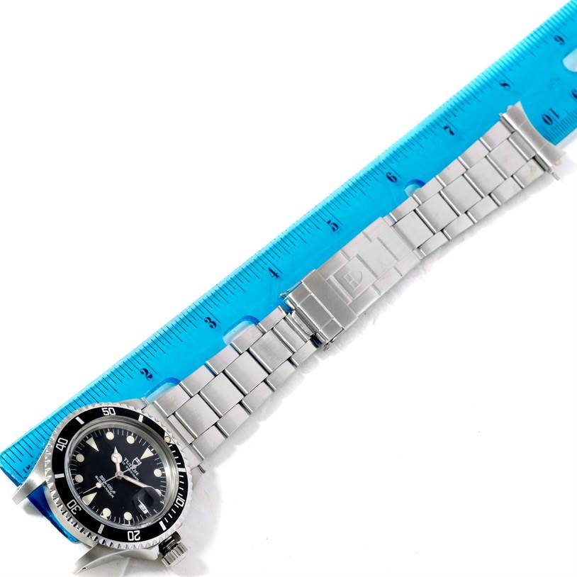 The image shows a Tudor Submariner 79090 Men's Stainless Steel Black Dial 79090 Men's Stainless Steel Black Dial watch laid flat beside a blue ruler, displaying the watch face and stainless steel bracelet.