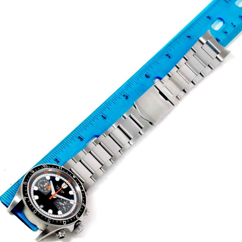 The Tudor Heritage Chrono 70330N-95740 Men's Stainless Steel Black Dial 70330N-95740 Men's Stainless Steel Black Dial watch is shown laid flat with its full metal bracelet, alongside a blue ruler for scale.