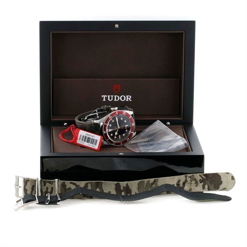 The image shows a Tudor Heritage Black Bay 79220R Men's Stainless Steel Black Dial 79220R Men's Stainless Steel Black Dial watch in its box with a camouflage strap and additional accessories.