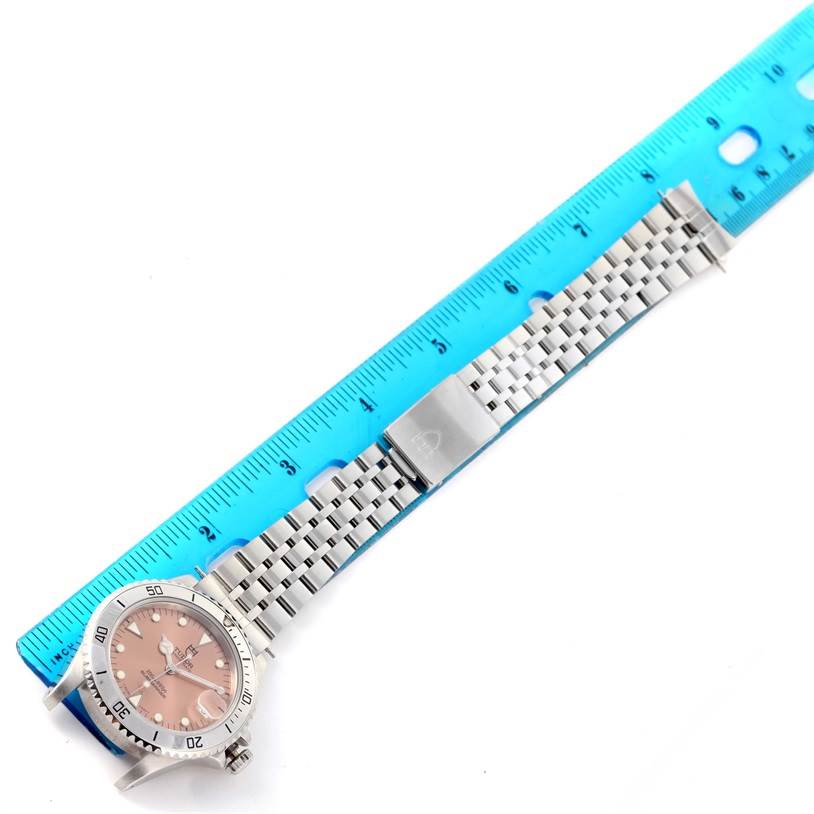 The Tudor Submariner 75190 Men's Stainless Steel Pink Dial 75190 Men's Stainless Steel Pink Dial watch is shown from a top-down angle alongside a blue ruler, highlighting the face and metal bracelet.