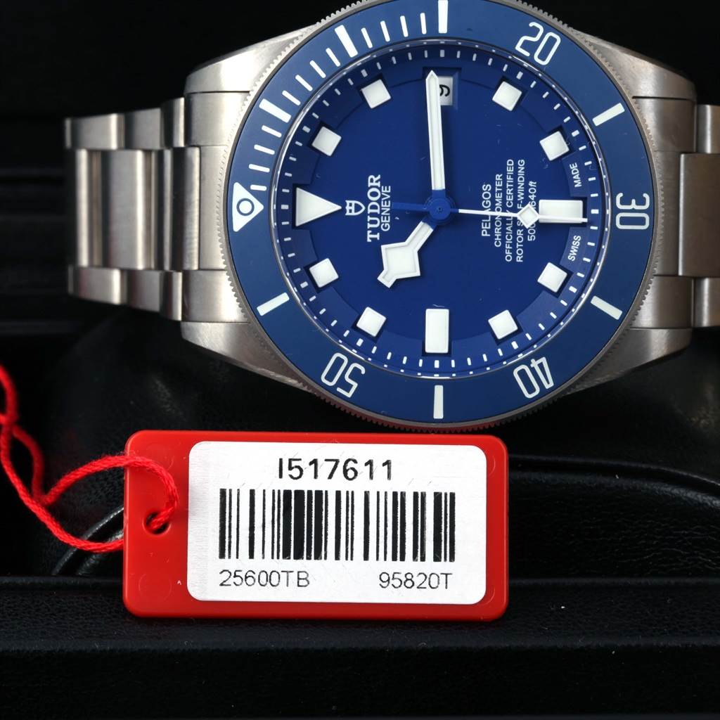 The Tudor Pelagos 25600TB Men's Titanium Blue Dial 25600TB Men's Titanium Blue Dial watch is shown from an angle focusing on the dial, bezel, and part of the bracelet with a tag displaying its model number.