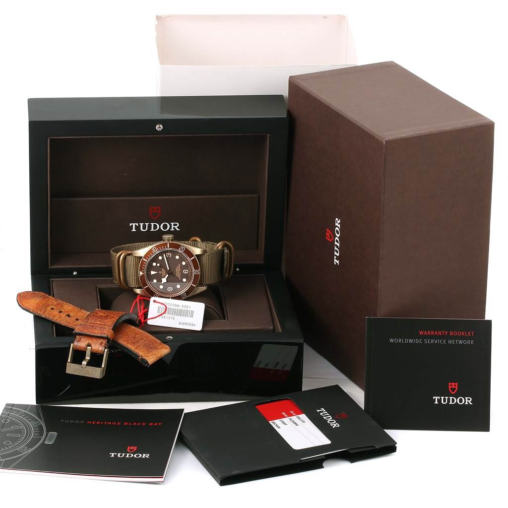 The image shows a Tudor Heritage Black Bay 79250 Men's Bronze Brown Dial 79250 Men's Bronze Brown Dial watch in its box, accompanied by an additional leather strap, warranty booklet, and promotional materials.