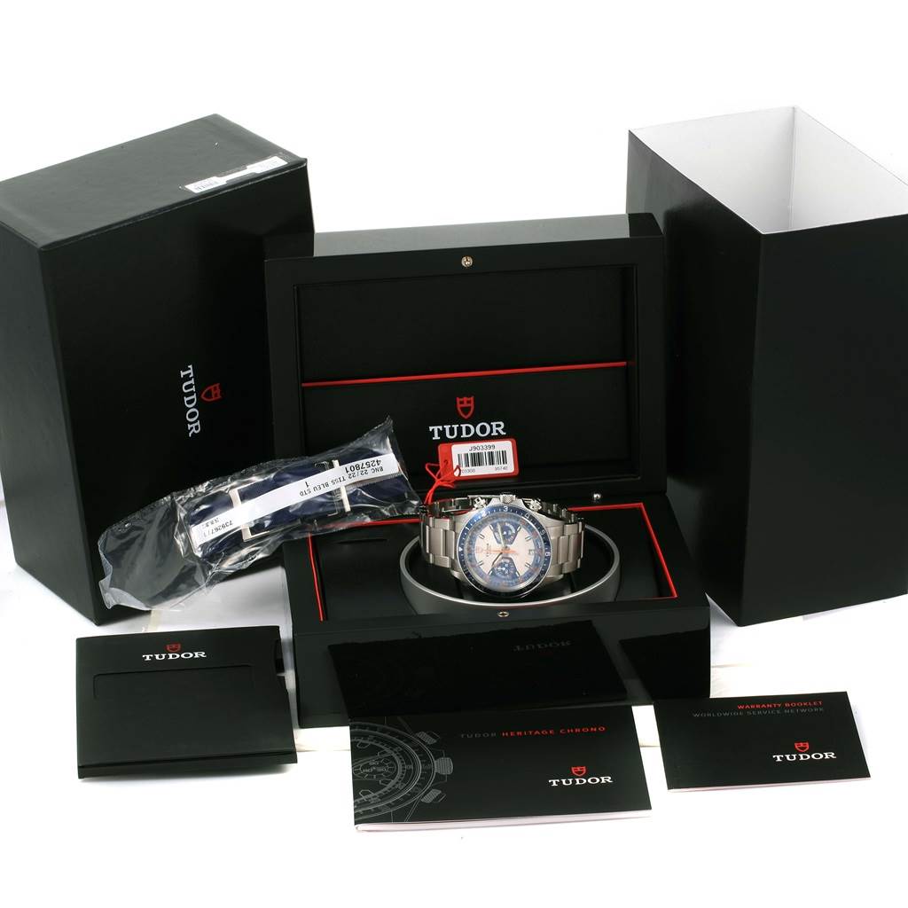 The image shows a Tudor Heritage Chrono 70330 Men's Stainless Steel Blue Dial 70330 Men's Stainless Steel Blue Dial watch with its packaging, warranty card, manuals, and an extra strap.
