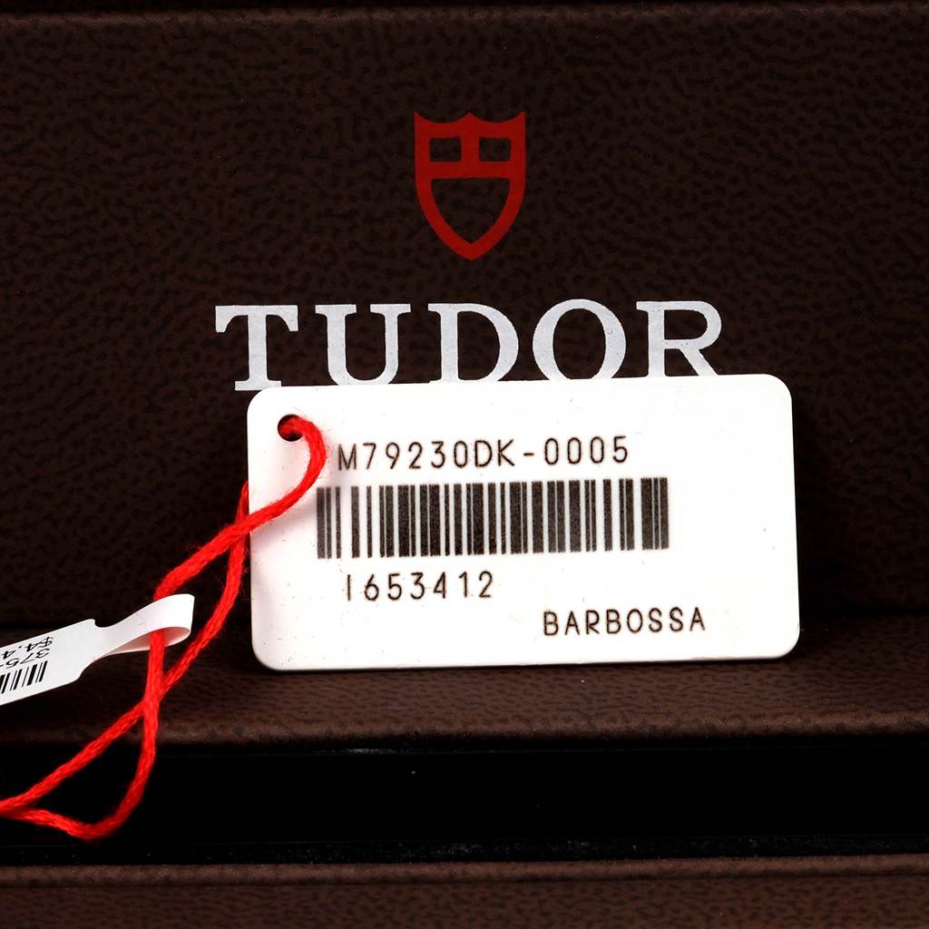 The image shows a close-up of a Tudor Heritage Black Bay 79230DK Men
s Stainless Steel Black Dial 79230DK Men
s Stainless Steel Black Dial model tag with a barcode and model number.