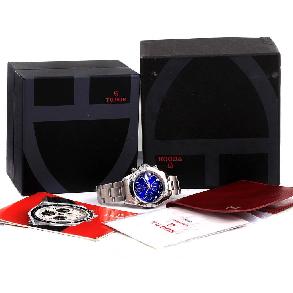 The Tudor Tiger 79280 Men's Stainless Steel Blue Dial 79280 Men's Stainless Steel Blue Dial watch is centered in front of its packaging, including manuals and booklets, viewed from the front.