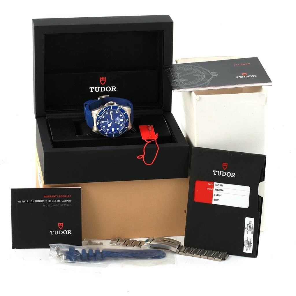 The image shows the Tudor Pelagos 25600 Men's Titanium Blue Dial 25600 Men's Titanium Blue Dial watch, its box, extra bracelet links, warranty booklet, and other accessories at an angled view.