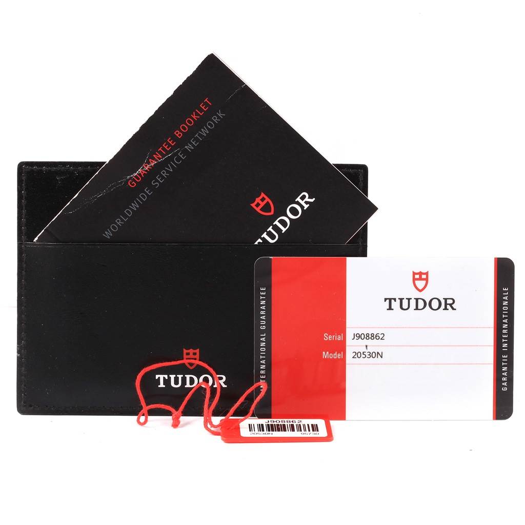 The image shows a Tudor Grantour 20530N-95730 Men's Stainless Steel Black Dial 20530N-95730 Men's Stainless Steel Black Dial model's guarantee booklet, international guarantee card, and a red hangtag from a frontal angle.