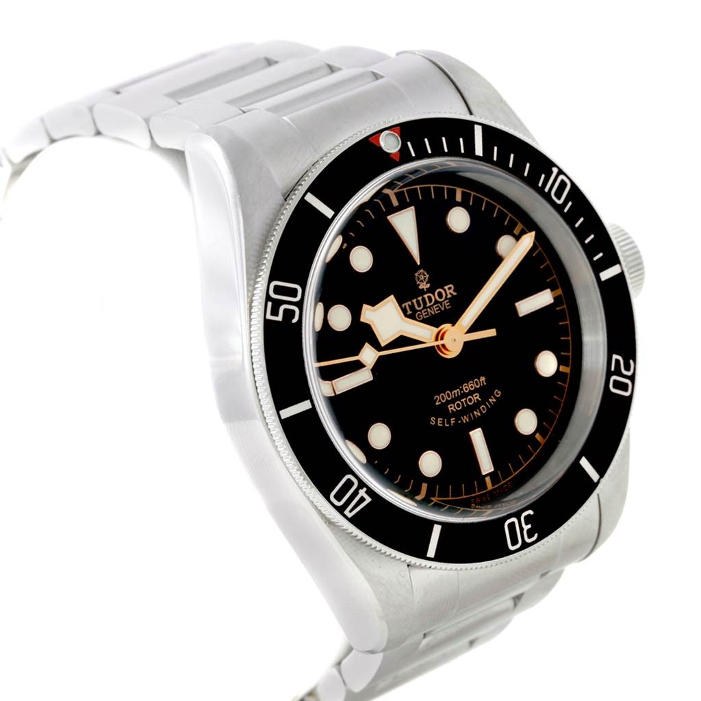 The Heritage Black Bay by Tudor is shown from a front-left angle, highlighting its black bezel, dial, indices, and stainless steel bracelet.