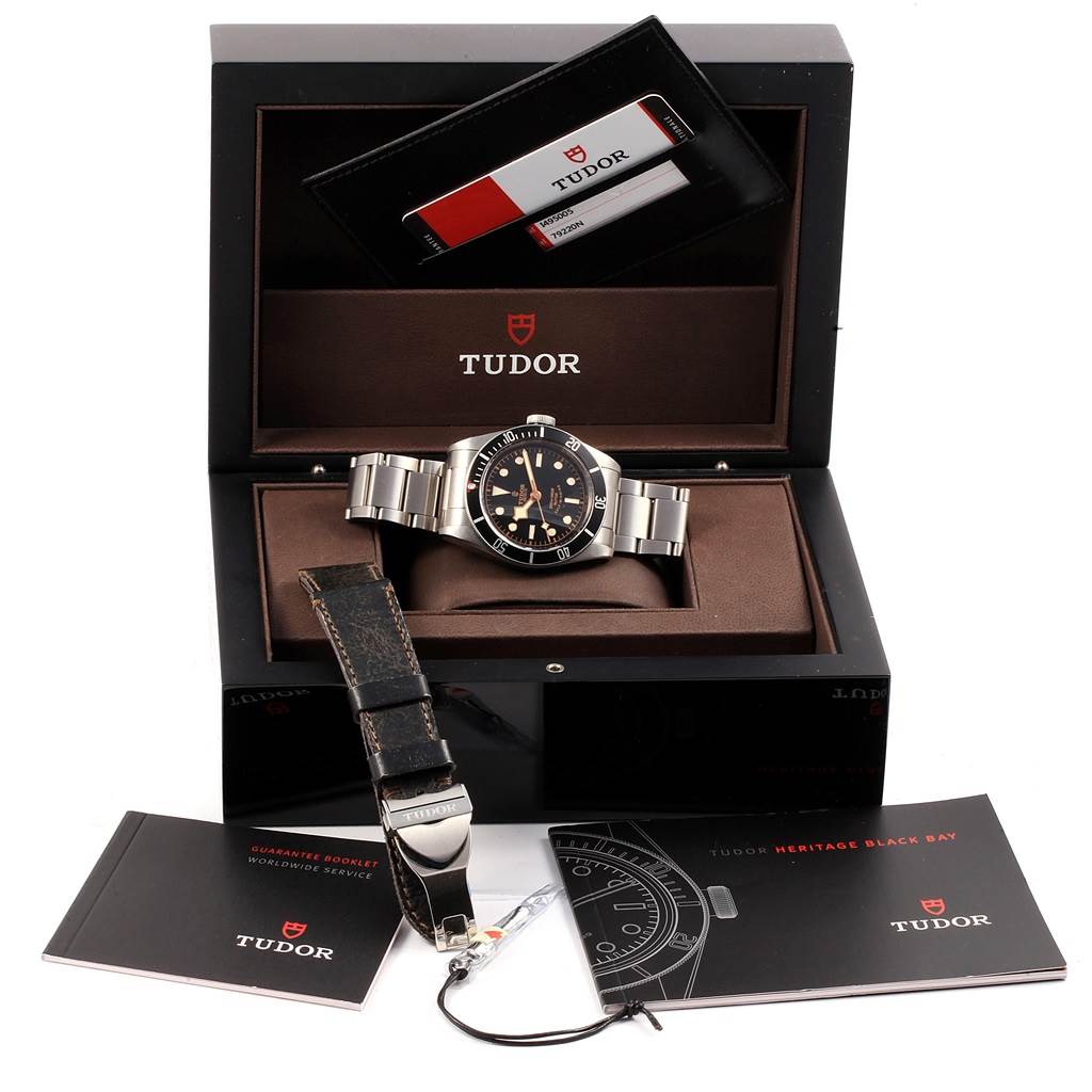 This image shows the Tudor Heritage Black Bay 79220N Men's Stainless Steel Black Dial 79220N Men's Stainless Steel Black Dial watch with its box, warranty card, booklet, and an additional strap.