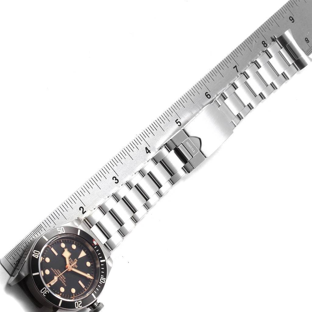 This image shows the Tudor Heritage Black Bay 79230N Men's Stainless Steel Black Dial 79230N Men's Stainless Steel Black Dial watch partially, focusing on its dial, bezel, and metal bracelet, alongside a ruler.