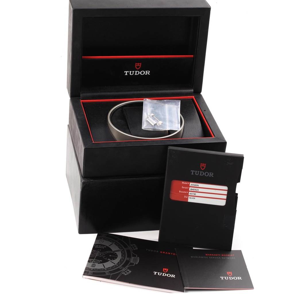 The image shows the Tudor Grantour 20500N Men's Stainless Steel Silver Dial 20500N Men's Stainless Steel Silver Dial watch's packaging, including its box, additional bracelet links, warranty card, and manual.