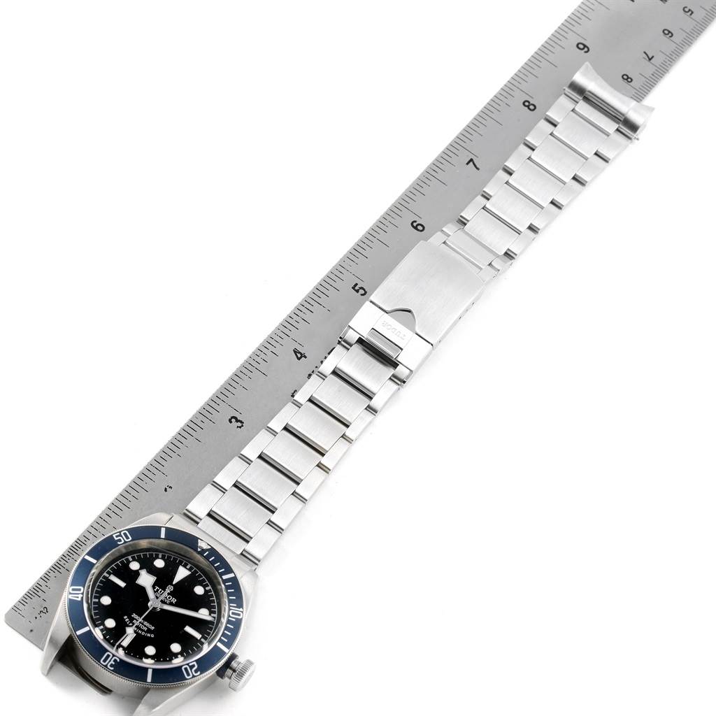 The image shows the Tudor Heritage Black Bay 79220 Men's Stainless Steel Black Dial 79220 Men's Stainless Steel Black Dial watch from a top-down angle, displaying the face, bezel, and stainless steel strap next to a ruler.