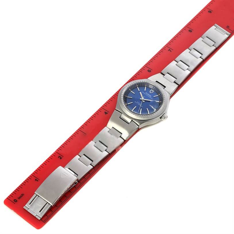 The Tudor Prince 9101/0 Men's Stainless Steel Blue Dial 9101/0 Men's Stainless Steel Blue Dial model watch is shown from the top, highlighting its face, bezel, and stainless steel bracelet next to a red ruler.