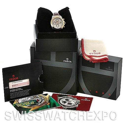 The image features a Tudor Tiger 79263 Men's Yellow Gold Champagne Dial 79263 Men's Yellow Gold Champagne Dial watch on a stand, along with its packaging, warranty card, instruction manuals, and a cleaning cloth.