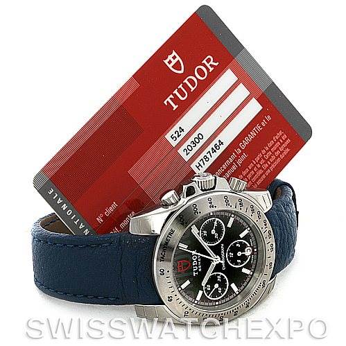 The image shows a Tudor Sport Chronograph 20300 Men's Stainless Steel Black Dial 20300 Men's Stainless Steel Black Dial watch from an angled side view, highlighting the bezel, pushers, crown, dial, and a warranty card.