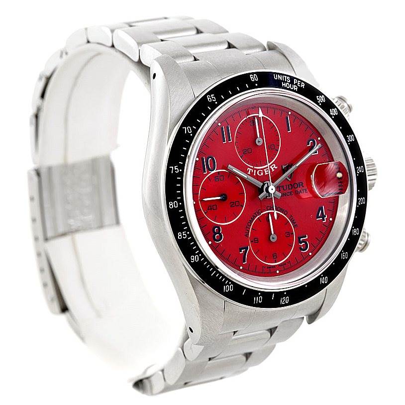 The image shows a Tudor Prince watch at an angle that displays the red dial, chronograph features, and stainless steel bracelet.