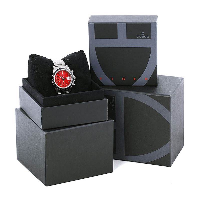 The image shows a Tudor Prince model watch with a red dial, presented in a box alongside additional packaging elements.