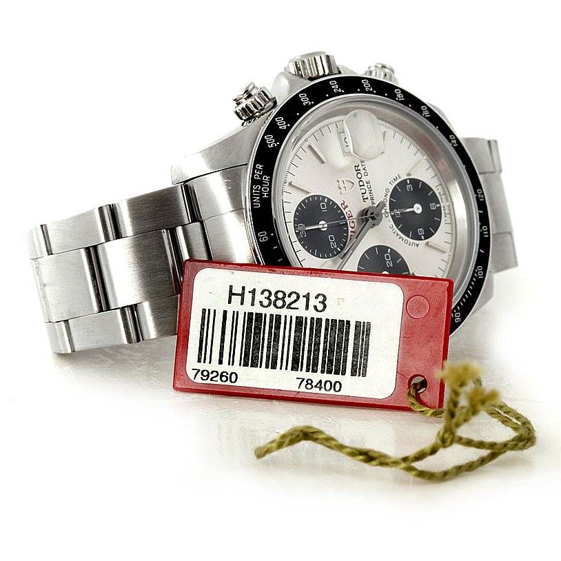 This image shows the Tudor Tiger 79260 Men's Stainless Steel Silver Dial 79260 Men's Stainless Steel Silver Dial wristwatch from a 3/4 angle, highlighting its dial, bezel, buttons, and metal bracelet, with a tag in the foreground.