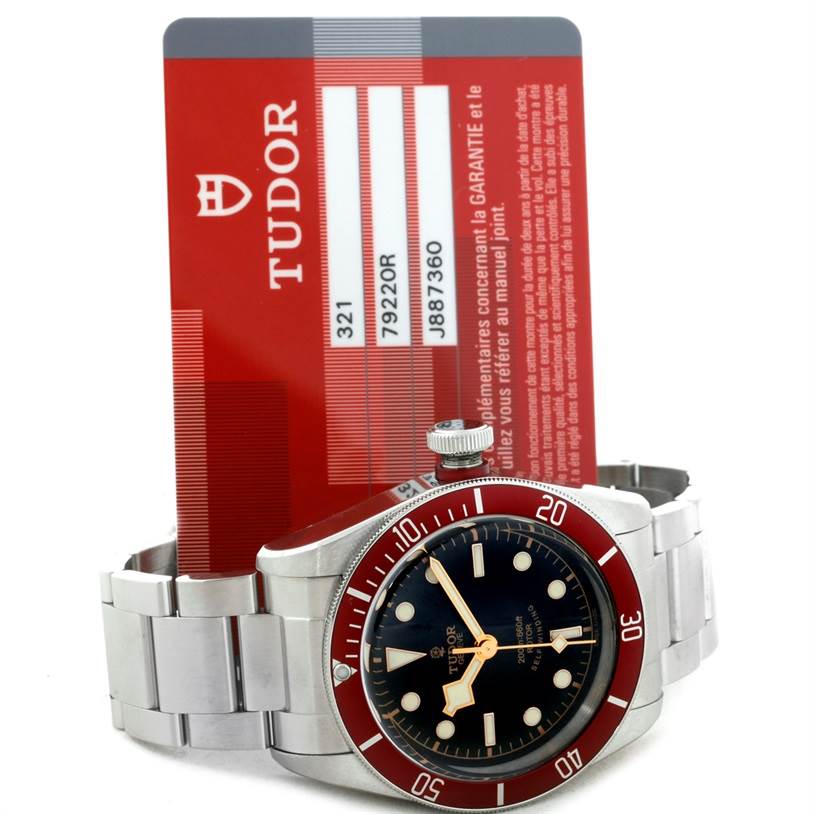 The image shows a Tudor Heritage Black Bay 79220 Men
s Stainless Steel Black Dial 79220 Men
s Stainless Steel Black Dial watch front view, including its face, bezel, and part of the bracelet, alongside its guarantee card.