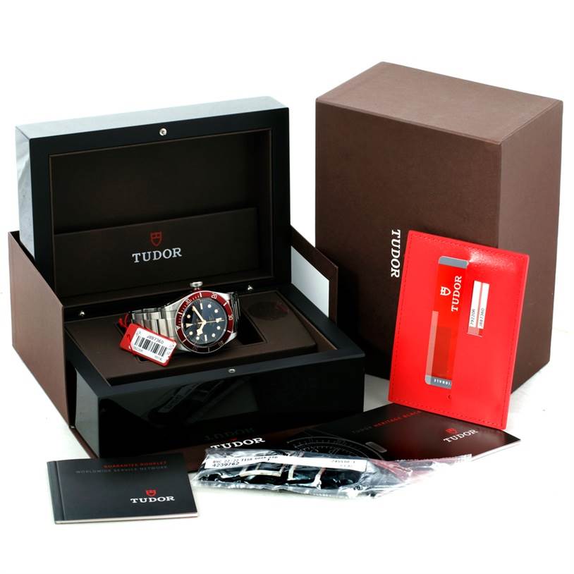 The image shows a Tudor Heritage Black Bay 79220 Men
s Stainless Steel Black Dial 79220 Men
s Stainless Steel Black Dial watch in its open box with additional accessories and documents.