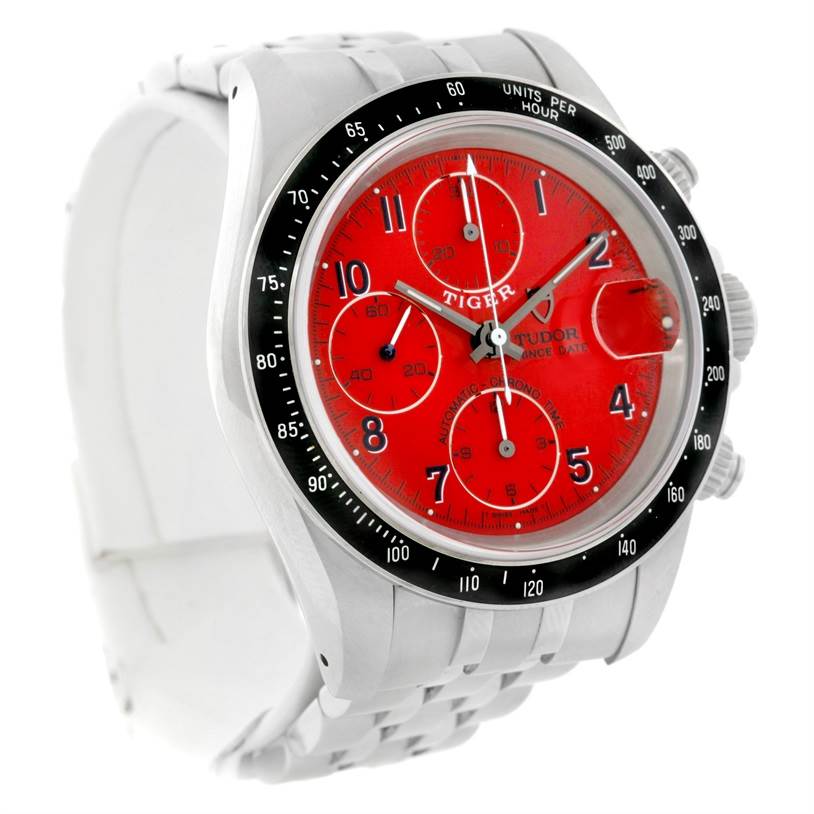 The image shows a Tudor Prince model watch at a three-quarter angle, displaying its red dial, chronograph subdials, and stainless steel bracelet.