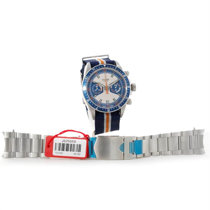 The image shows a front view of the Tudor Heritage Chrono 79220R Men's Stainless Steel Blue Dial 79220R Men's Stainless Steel Blue Dial watch and a stainless steel bracelet with a tag attached.