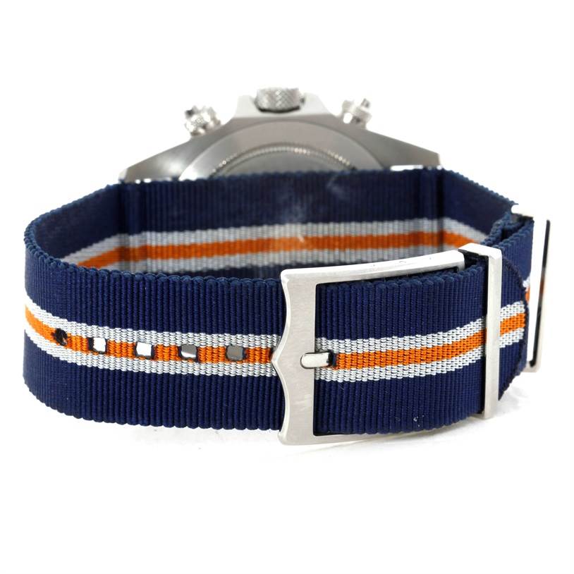 The image shows the back of a Tudor Heritage Chrono 79220R Men's Stainless Steel Blue Dial 79220R Men's Stainless Steel Blue Dial watch with a blue, orange, and white-striped strap and a silver buckle.
