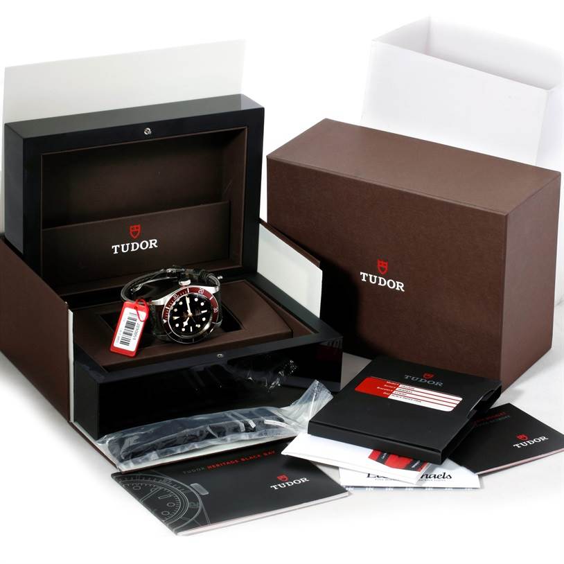 The image shows an unboxing of the Tudor Heritage Black Bay 79220R Men's Stainless Steel Black Dial 79220R Men's Stainless Steel Black Dial watch, including its box, manual, warranty card, and additional straps.